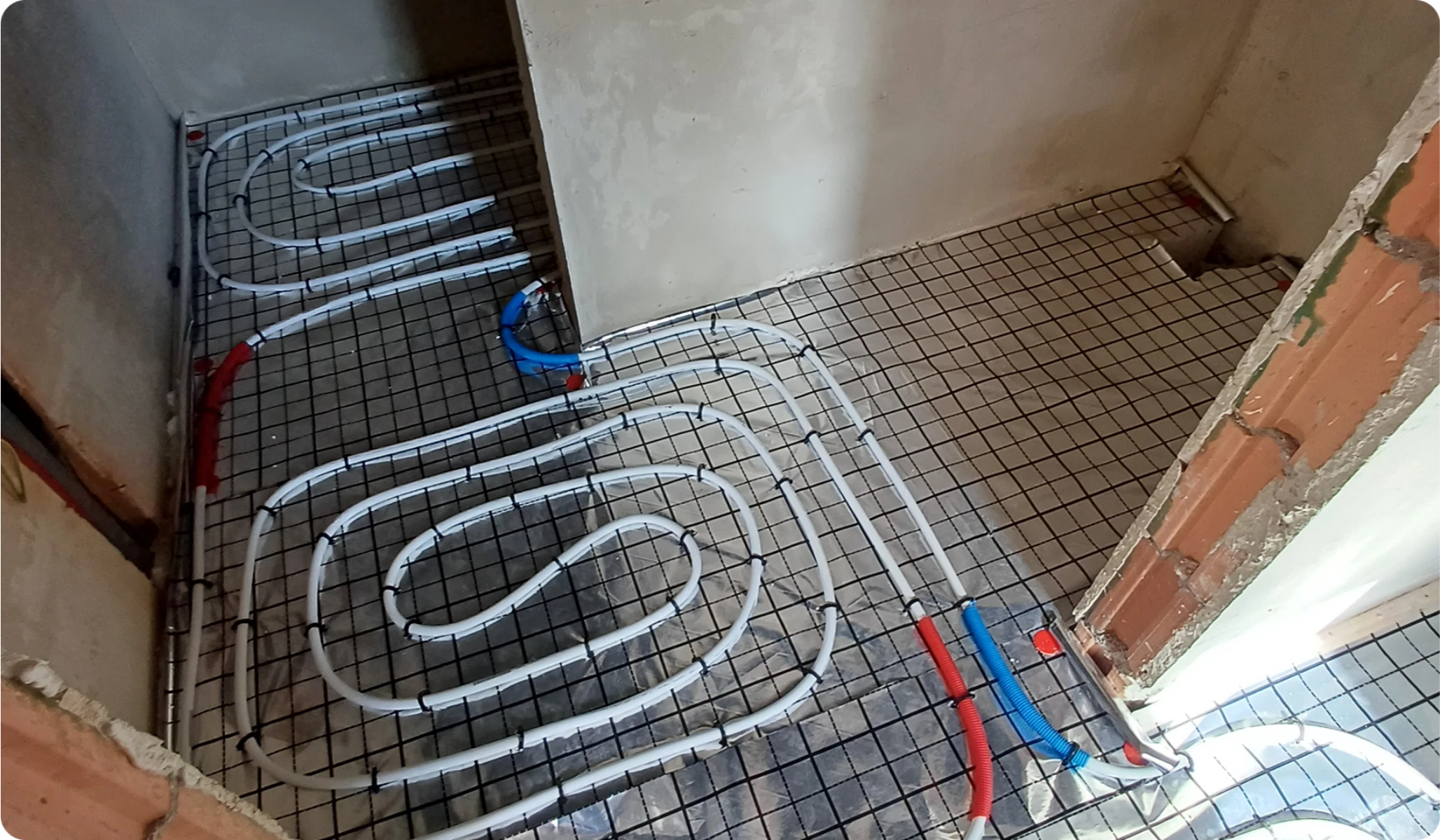 Rozłożona instalacja ogrzewania podłogowego z białymi rurami na stalowej siatce zbrojeniowej