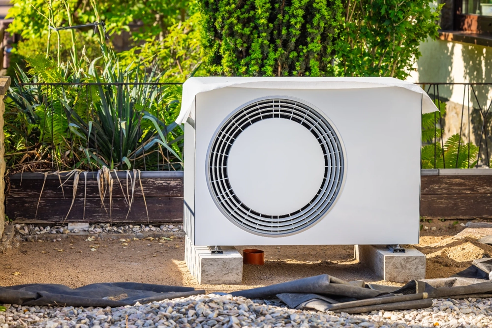 Jednostka zewnętrzna pompy ciepła na podłożu kamiennym obok roślin